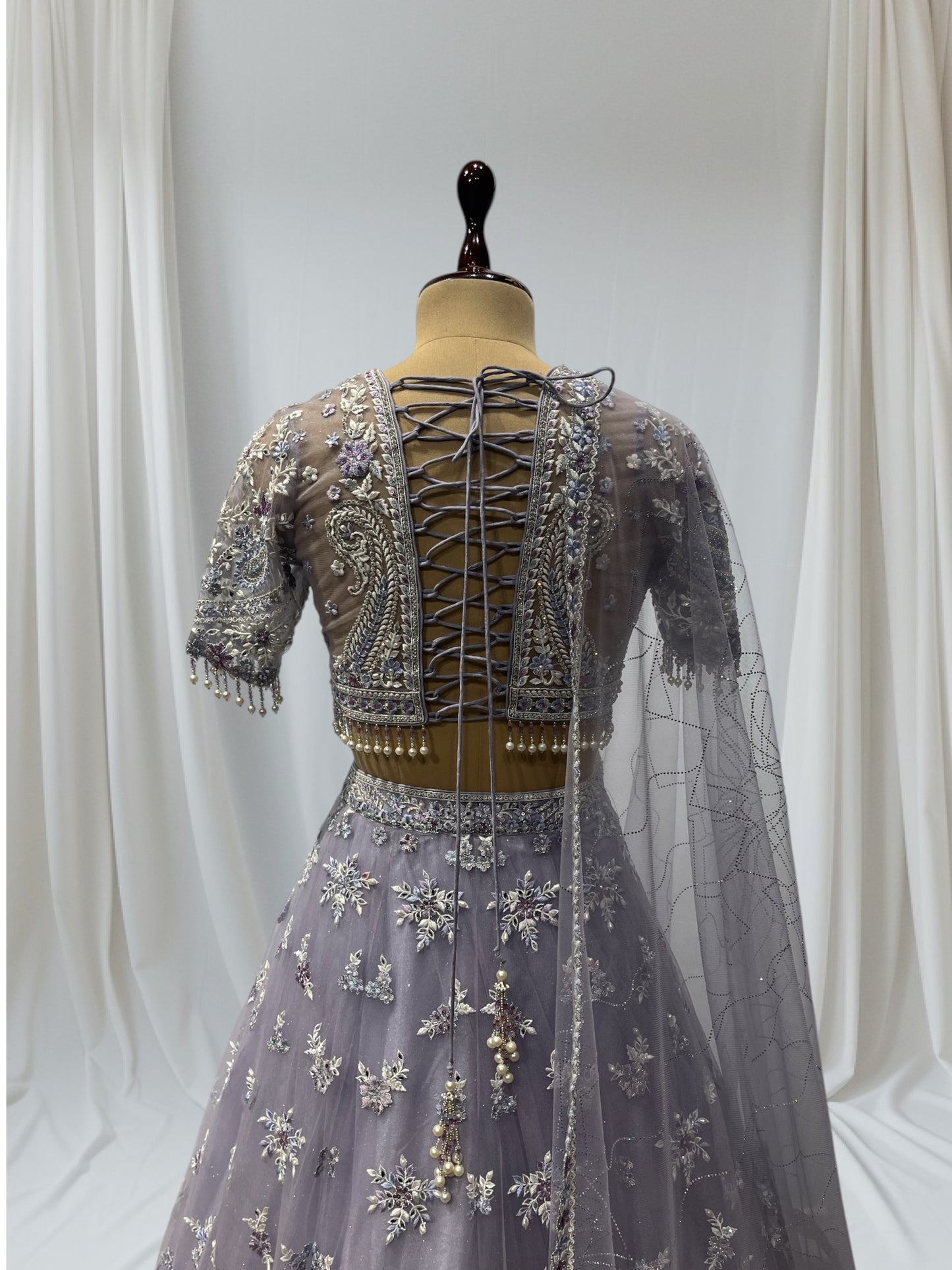 LAVENDER COLOR PAIRED WITH A CROP TOP CRAFTED DORI  AT THE BACK, FROM NET FABRIC IT FEATURES INTRICATE THREAD EMBROIDERY WITH MIRROR WORK AND PEARLS