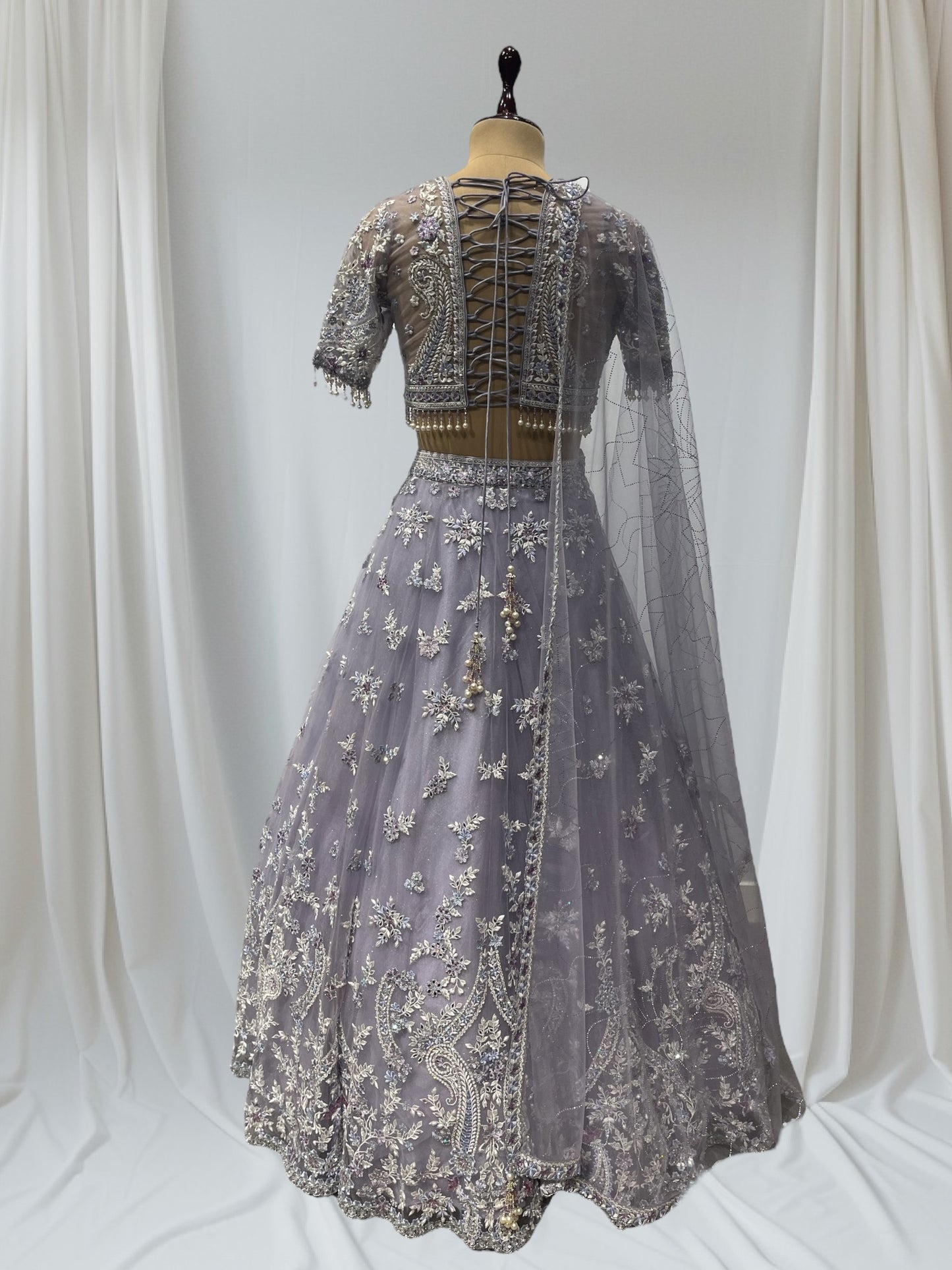 LAVENDER COLOR PAIRED WITH A CROP TOP CRAFTED DORI  AT THE BACK, FROM NET FABRIC IT FEATURES INTRICATE THREAD EMBROIDERY WITH MIRROR WORK AND PEARLS